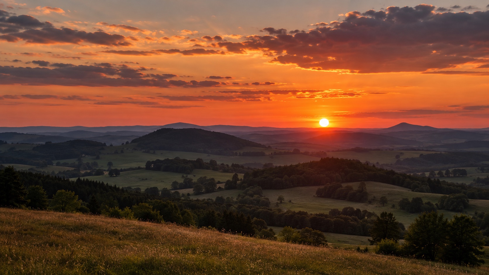 Červený a oranžový západ slunce nad kopci